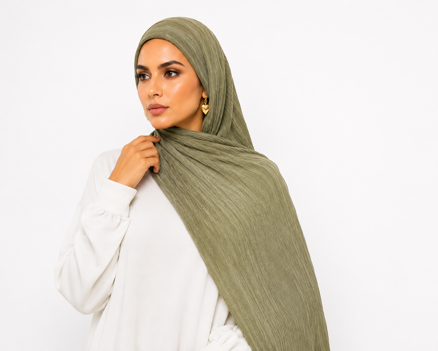 A woman wearing a textured sage green hijab and a white long-sleeve top, posing against a solid white background.